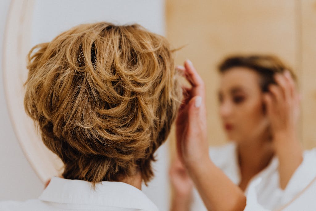 Back view of a woman styling her short hair while looking in the mirror.
