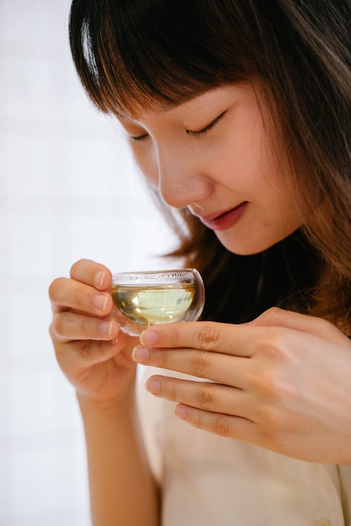 Young woman savoring the scent of green tea, eyes closed, indoors.
