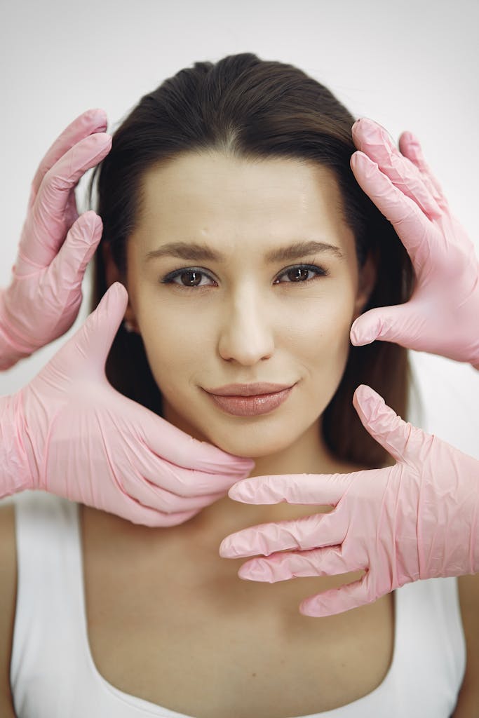 Close-up of a woman receiving a skincare treatment with pink gloves indoors.