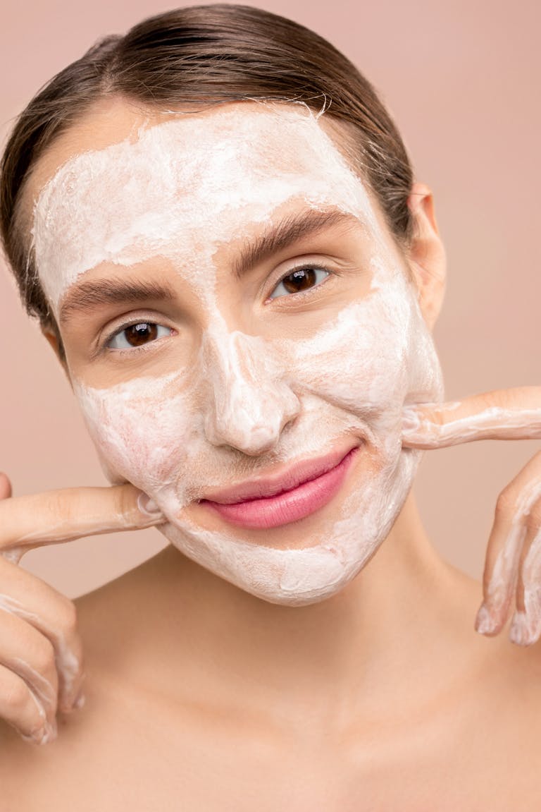 Woman with white facial foam smiling, showcasing skincare routine indoors.