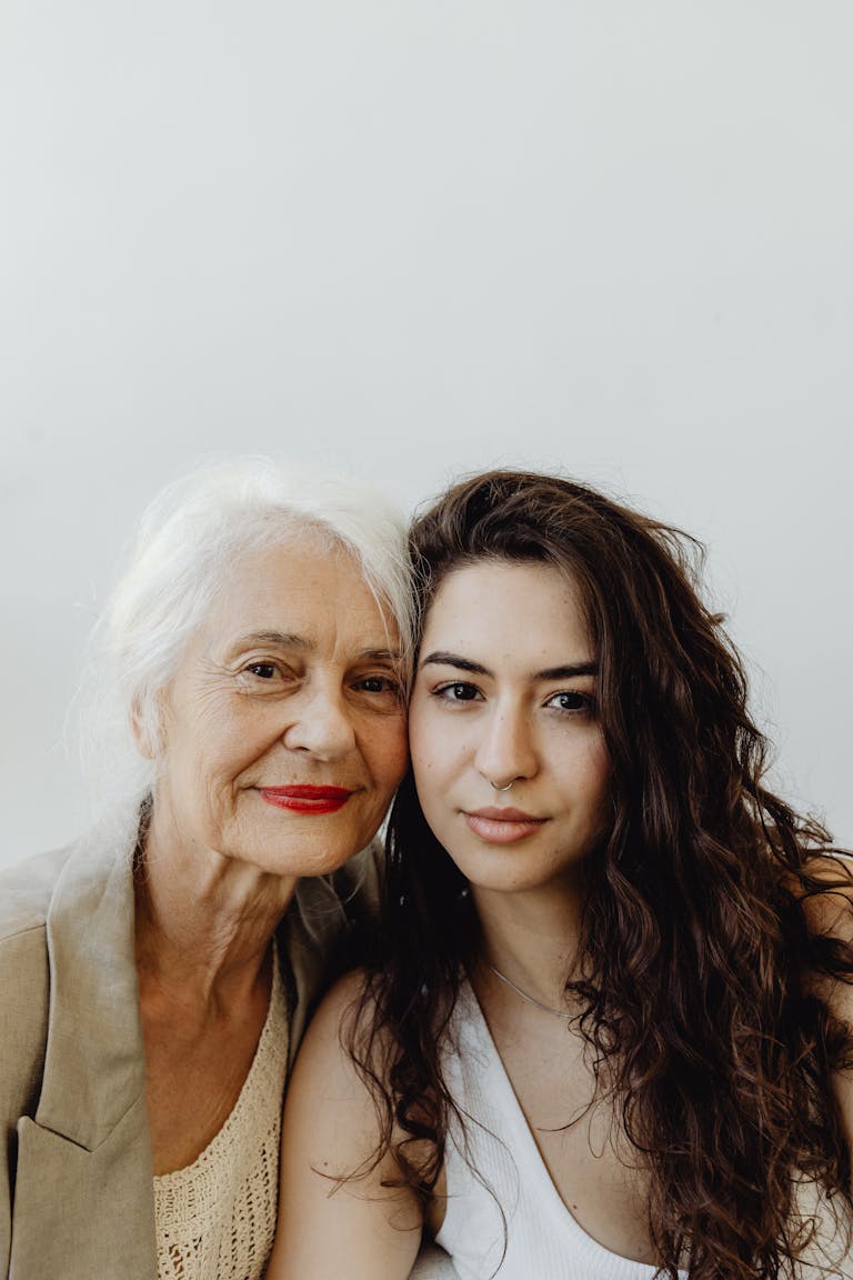 Intimate portrait of a grandmother and granddaughter smiling warmly against a white background.