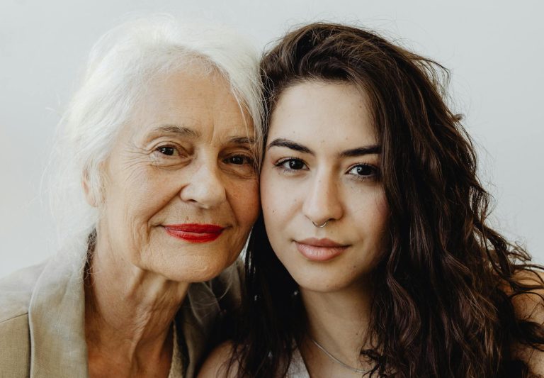Intimate portrait of a grandmother and granddaughter smiling warmly against a white background.