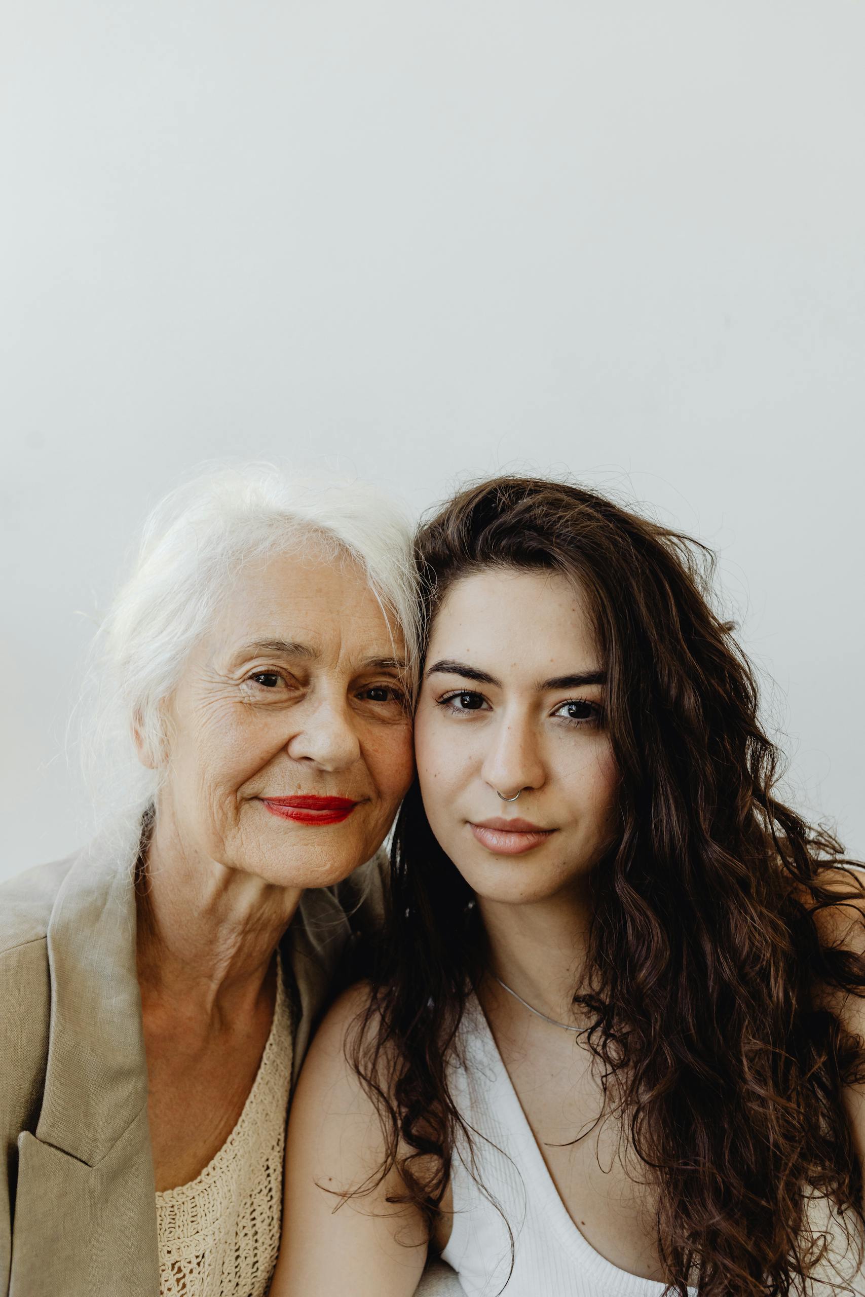 Intimate portrait of a grandmother and granddaughter smiling warmly against a white background.