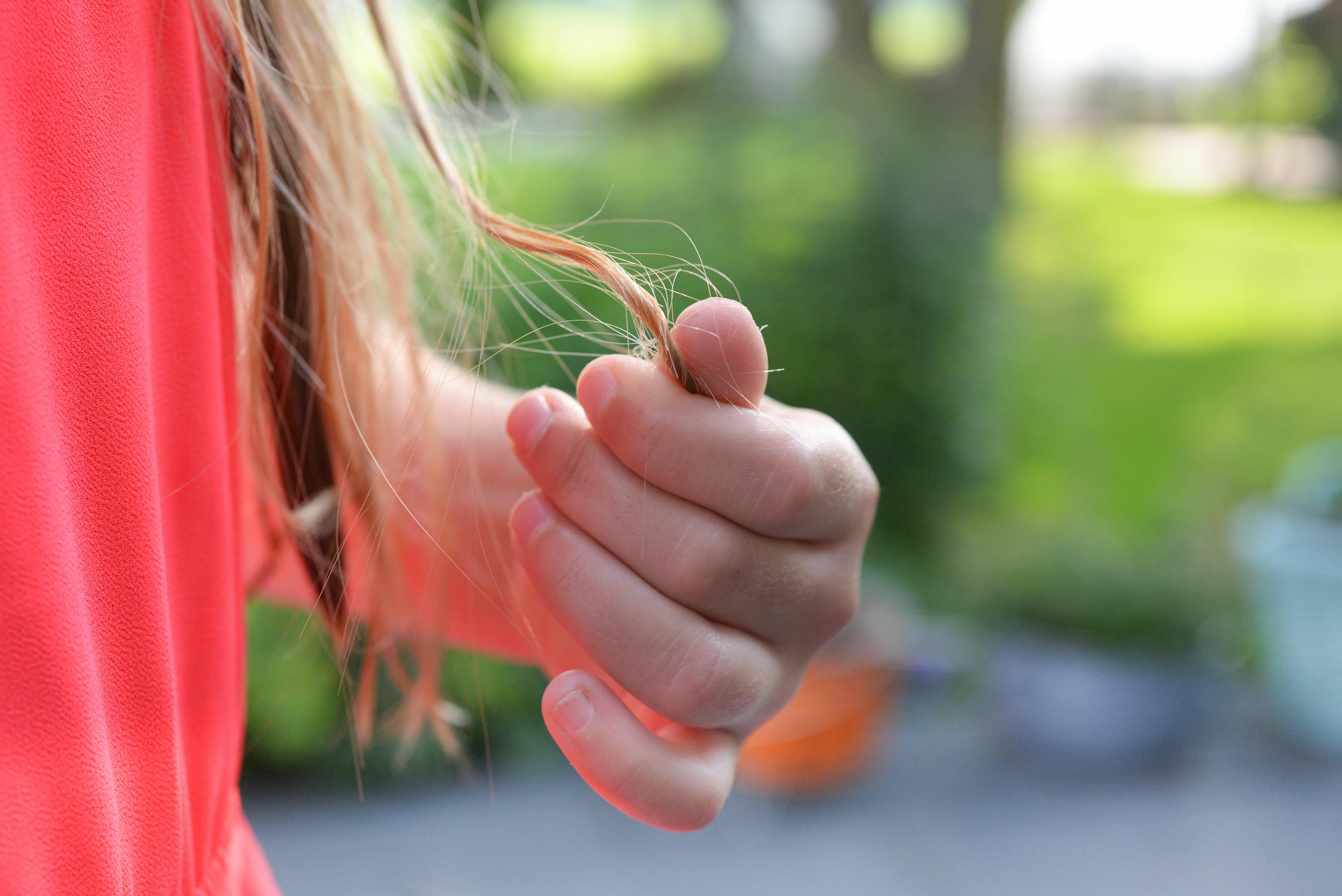 A young girl gently holds a strand of hair, showcasing a serene outdoor moment.