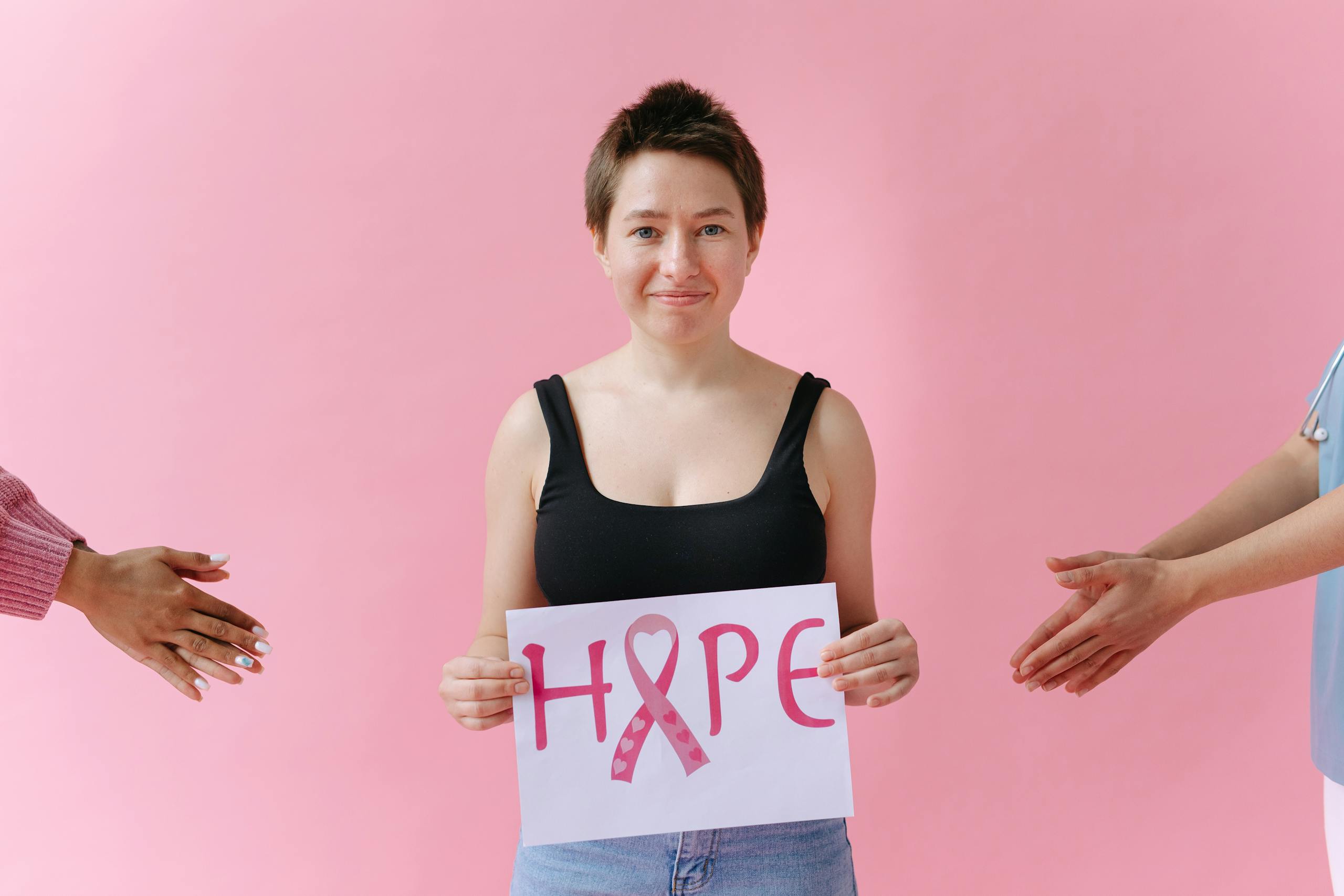 A young woman holds a pink ribbon hope sign promoting breast cancer awareness in a studio.