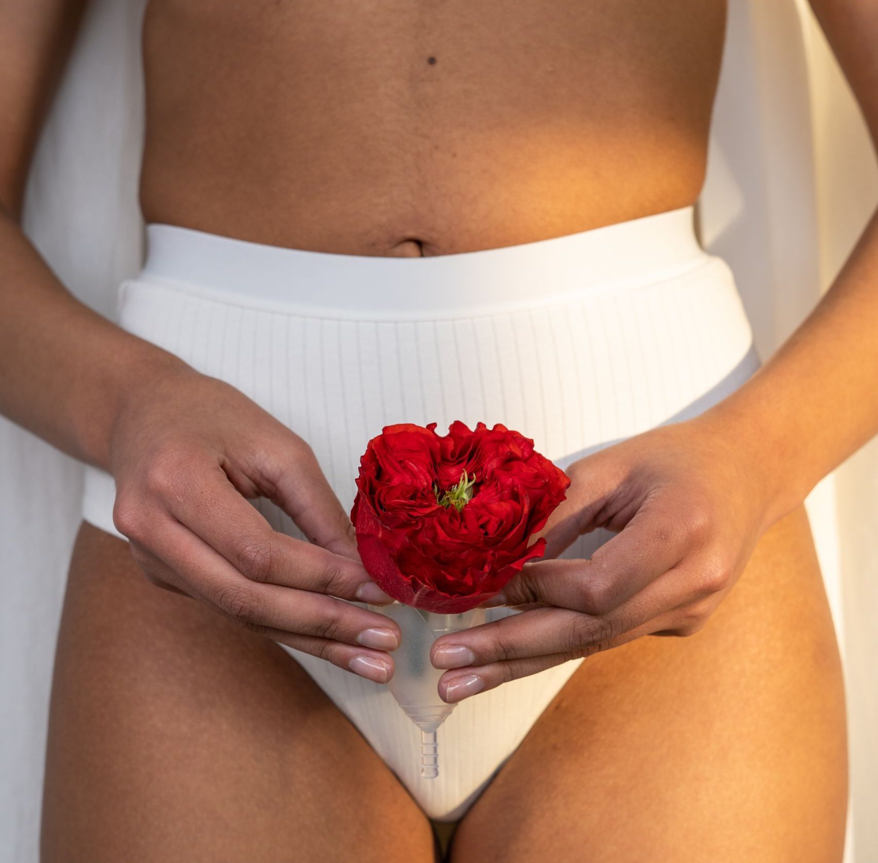 Woman holding a red rose with a menstrual cup, symbolizing feminine hygiene.