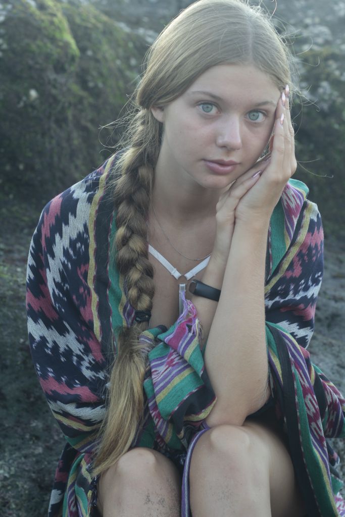 Portrait of a young woman with long braid wrapped in colorful scarf sitting outdoors.